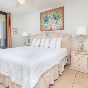 Master bedroom featuring a king bed with plush white bedding and a stunning view of the beach from the balcony