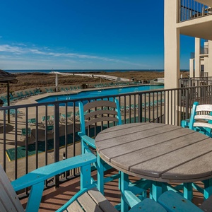 Balcony seating overlooks the pool area and offers a glimpse of the tranquil beach beyond, perfect for relaxation