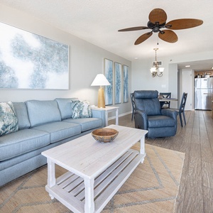 Bright living area features a light blue sofa, decorative pillows, and a cozy dining space with a view of the modern kitchen