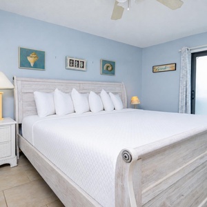 This bedroom features light blue colors, a cozy bed with plush pillows, and a serene view through the sliding glass door