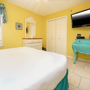 Cozy guest bedroom featuring a queen bed, turquoise accent furniture, and a wall-mounted TV