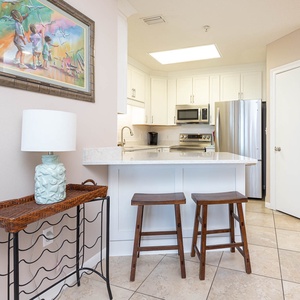 Enjoy casual dining at the breakfast bar with two wooden stools, complemented by a vibrant coastal artwork nearby