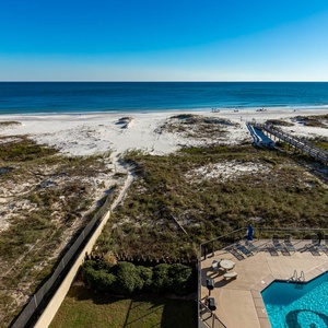 Expansive view of the beach and turquoise gulf waters from the balcony, with a pool area and boardwalk leading to the beach