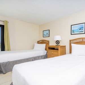 This bedroom features two comfortable beds and a large window offering a view of the palm-lined beachfront