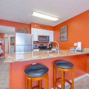 The kitchen features vibrant walls, granite countertops, stainless appliances, and bar seating for a cheerful experience