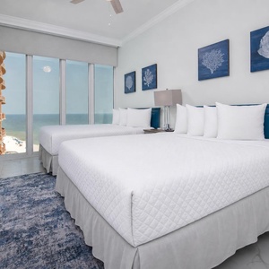 Wake to gulf light through floor-to-ceiling windows in this queen guest suite with coastal decor