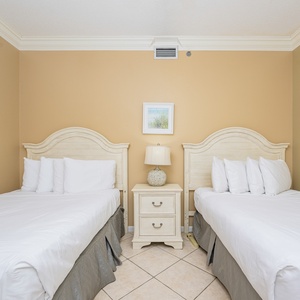 Brightly decorated guest bedroom featuring two double beds, a nightstand with a lamp, and coastal artwork on the walls