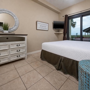 Cozy master bedroom features a comfortable king bed, stylish dresser, and a view of the beach from the patio