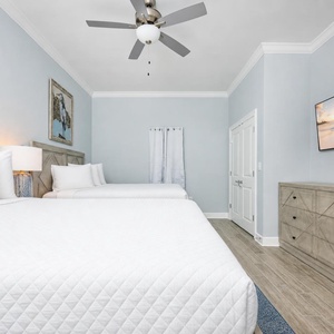 Relax in this serene guest bedroom featuring two queen beds, stylish decor, and a large TV for your favorite shows