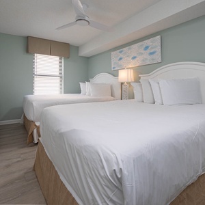 Rest in the inviting guest bedroom featuring two queen beds, a TV, and soft decor for a relaxing stay