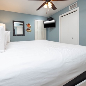 A cozy bedroom features a king bed with crisp white linens, a wall-mounted TV, and charming fish décor