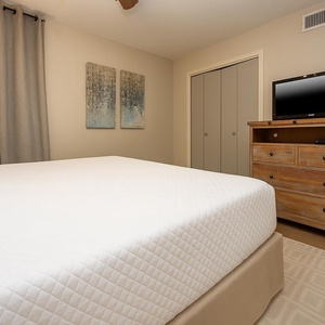 Cozy guest bedroom featuring a king bed, stylish artwork, and a rustic dresser with a TV