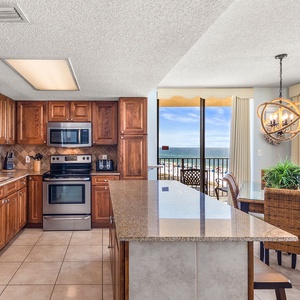 The modern kitchen features rich wooden cabinetry, a breakfast bar with seating, and a stunning view of the beach