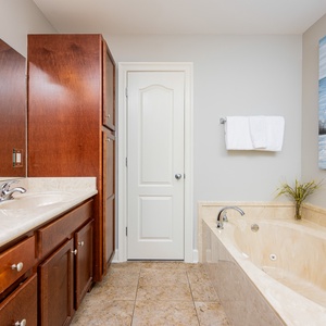 The master bath features a relaxing jetted tub, elegant wood cabinetry, and a serene coastal-themed artwork