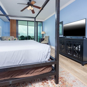 Spacious master bedroom featuring a four-poster king bed, cozy seating, and a view of the balcony beyond