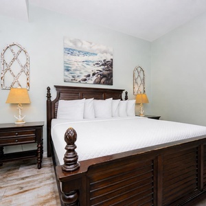 A cozy bedroom features a king bed with white linens, dark wood furniture, and nautical decor, creating a tranquil atmosphere