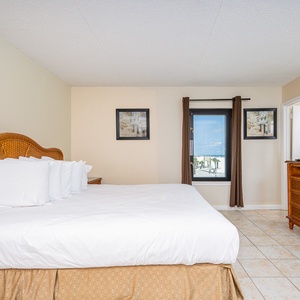 This bedroom features a plush bed and a window showcasing a beautiful beachfront view