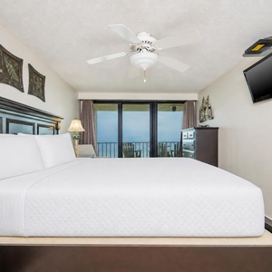 This bedroom features a plush bed, a wall-mounted TV, and a serene view from the balcony, perfect for relaxation