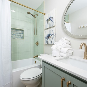 Guest bath featuring a tub/shower combo, light green tile, and decorative sea-themed artwork, complemented by fresh towels