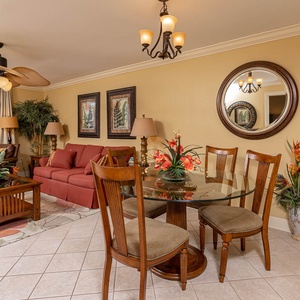 Living area features a red sofa with queen sleeper, glass dining table, and vibrant tropical decor, with a balcony beach view