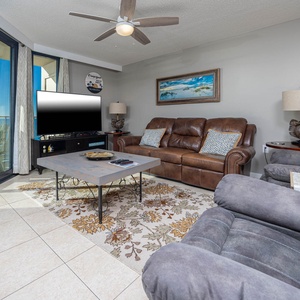 The inviting living area features a brown leather sofa with decorative pillows, a stylish coffee table, and a large TV