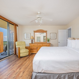 Bright and airy master bedroom features a king bed, wooden furniture, and a cozy chair, leading to the balcony