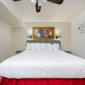 The bedroom features a large king bed with white linens, decorative pillows, and artwork above the headboard