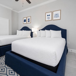Drift off on one of two fluffy queen beds beneath navy headboards and a lamp's warm glow in this guest suite