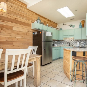 The inviting kitchen features mint green cabinetry, a rustic wooden dining table, and a cozy breakfast bar with stools
