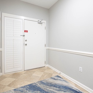 Welcoming entryway featuring a light gray wall, decorative trim, and a stylish blue area rug on tiled flooring