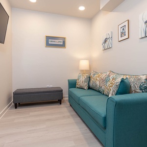 This relaxing area features a vibrant teal sofa with decorative pillows, a mounted TV, and artful marine-themed decor
