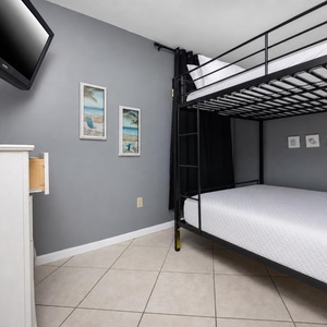 Guest bedroom featuring a cozy queen bunk bed, flat-screen TV, and beach-themed decor for a relaxing getaway