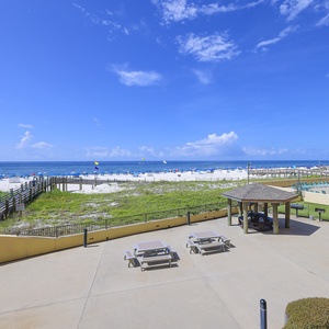 A view of the beach front showcases white sand, colorful umbrellas, and a gazebo beside the pool area under a bright blue sky