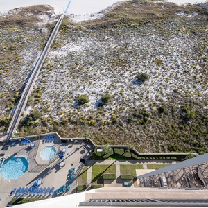 View of the pool area with lounge chairs and pathways leading through landscaped grounds to the beach beyond