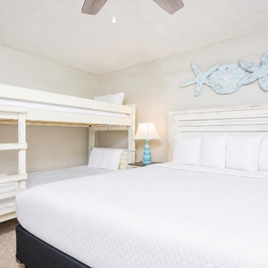 This cozy bedroom features a charming twin bunk bed and a queen bed, accented by beach-themed decor and soft lighting