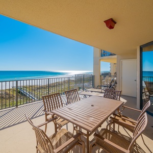 Spacious extended balcony with a wooden dining set offers a breathtaking view of the beach and turquoise waters beyond