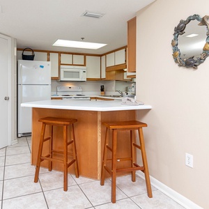 Kitchen area features a breakfast bar with two wooden stools, surrounded by light cabinetry and modern appliances