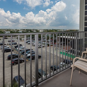 Master balcony with two chairs offers a view of the surrounding area, including parked cars and distant greenery