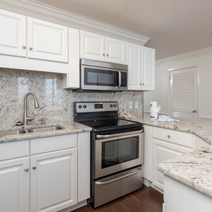 This modern kitchen features sleek white cabinetry, granite countertops, and a convenient breakfast bar for casual dining