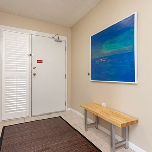 Welcoming entryway features a wooden bench, vibrant blue artwork, and tile flooring, creating a bright and inviting vibe