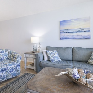 The living area features a blue and white color scheme, comfortable seating, and beach-themed decor for a relaxing getaway