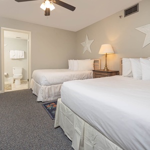 Brightly decorated bedroom featuring two double beds, and a cozy nightstand with a lamp, leading to the en-suite bathroom