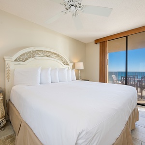 Bright master bedroom featuring a king bed, elegant furnishings, and a sliding door leading to the balcony with beach views