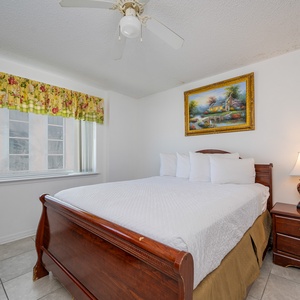 The master bedroom features a queen bed with floral bedding, a TV, and a lovely view from the large window