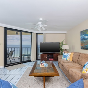 The living room features a cozy sofa with queen sleeper, a wooden coffee table, and large windows showcasing a beach view
