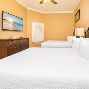 White linens cover two queen beds in this guest suite where you unwind and watch shows on the flat screen TV