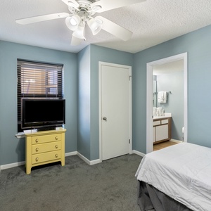 A cozy guest bedroom features a two twin beds, a yellow dresser with a TV, and an adjoining bathroom