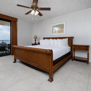 Unwind in the spacious master bedroom, featuring a king bed, warm wood accents, and beachfront balcony access