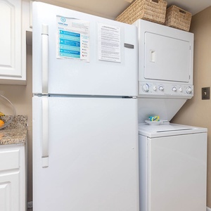This kitchen features white cabinetry, a full-size refrigerator, and a convenient stacked washer and dryer for easy living