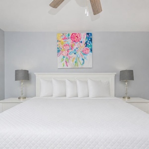 This bedroom features a large white bed with plush pillows, stylish lamps, and colorful artwork, creating a serene atmosphere